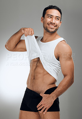 Buy stock photo Shot of a handsome young man standing alone in the studio and lifting up his shirt to show his abs