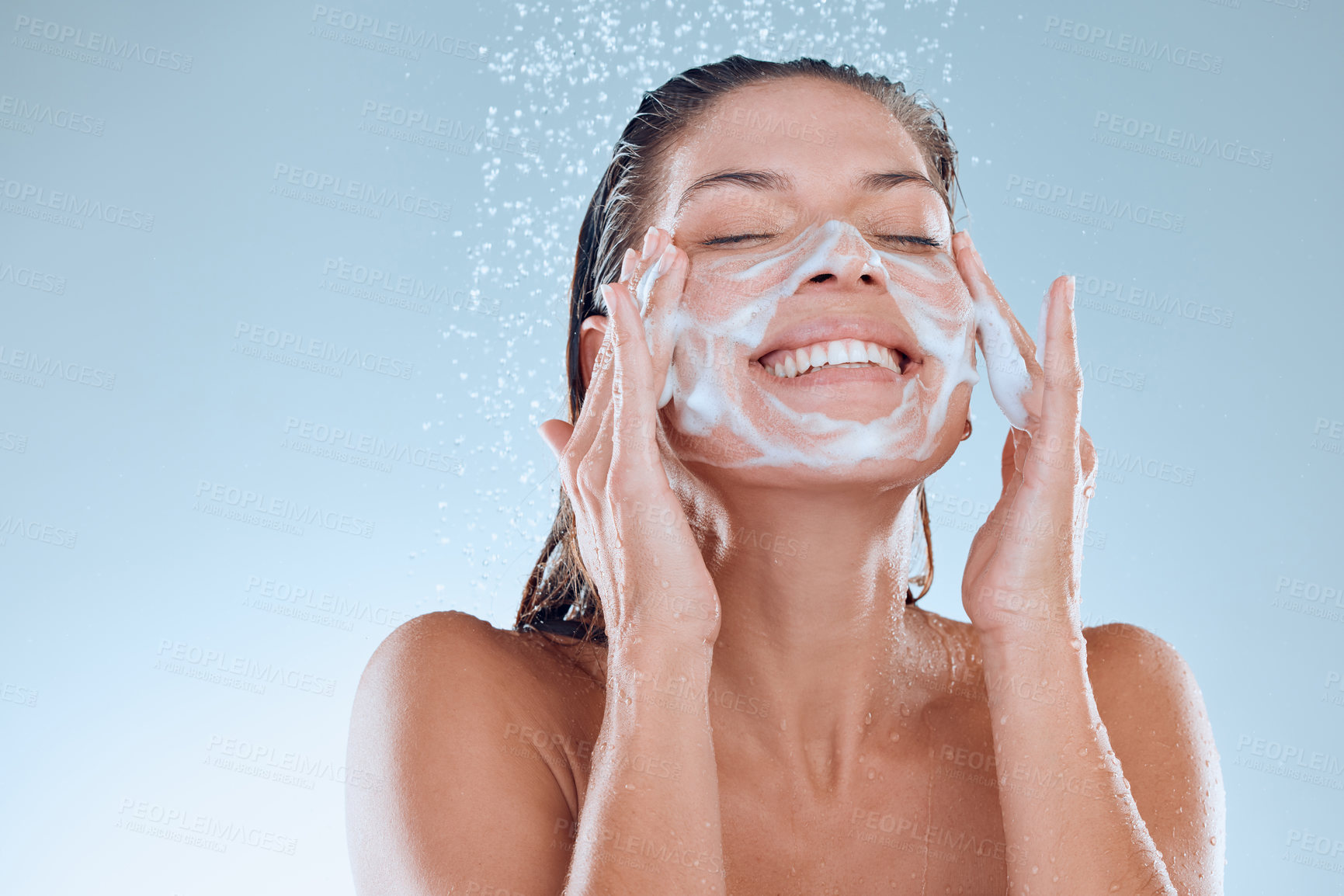 Buy stock photo Woman, facial and soap for skincare hygiene with foam, wash or clean against blue studio background. Happy, splash and model person for body wellness, cosmetics or healthy skin treatment in water