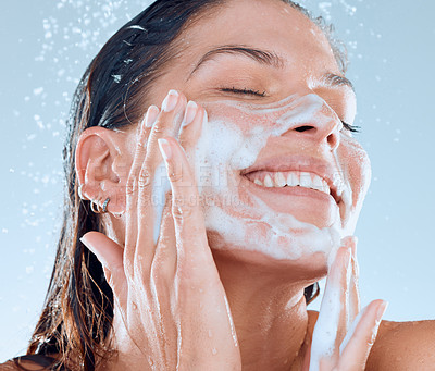 Buy stock photo Studio shot of a young woman washing her face while taking a shower against a blue background