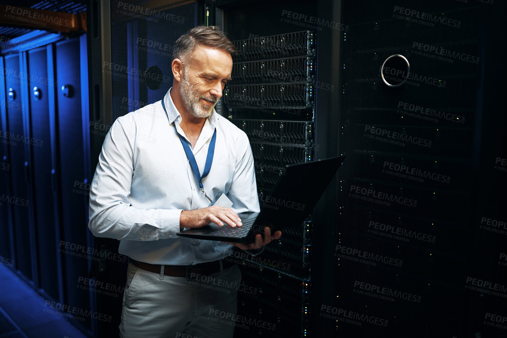 Buy stock photo Shot of a mature man using a laptop while working in a server room