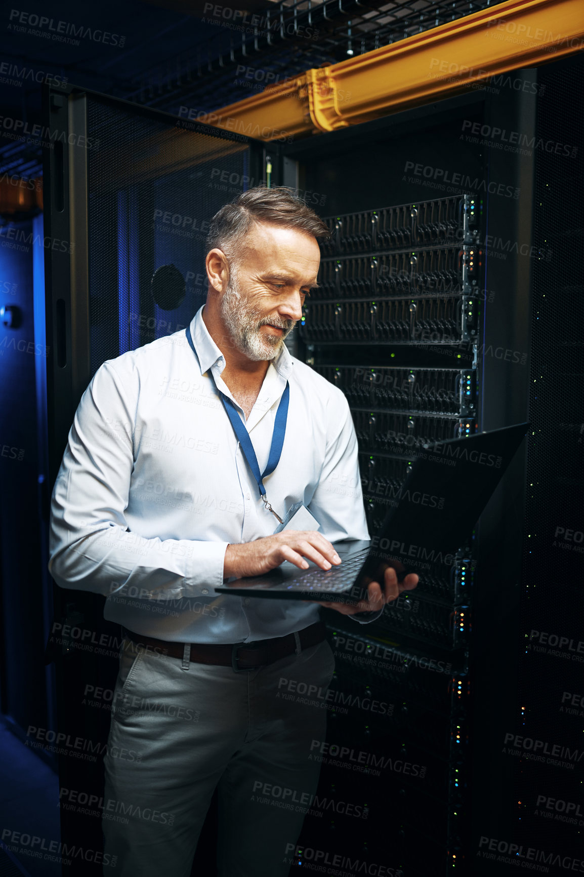 Buy stock photo Shot of a mature man using a laptop while working in a server room