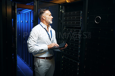 Buy stock photo Shot of a mature man using a laptop while working in a server room