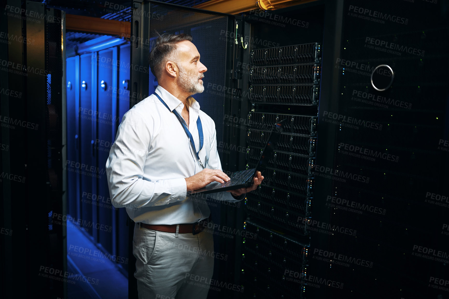 Buy stock photo Shot of a mature man using a laptop while working in a server room