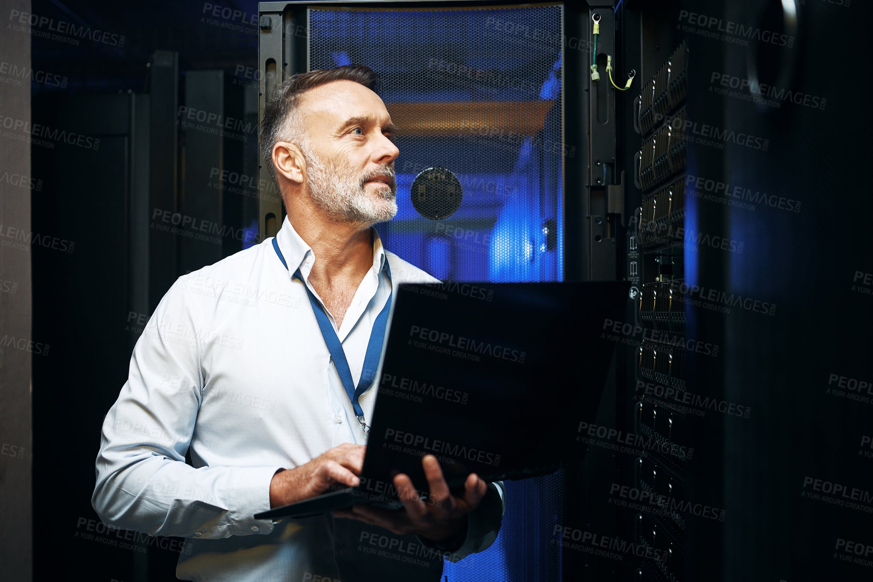 Buy stock photo Shot of a mature man using a laptop while working in a server room