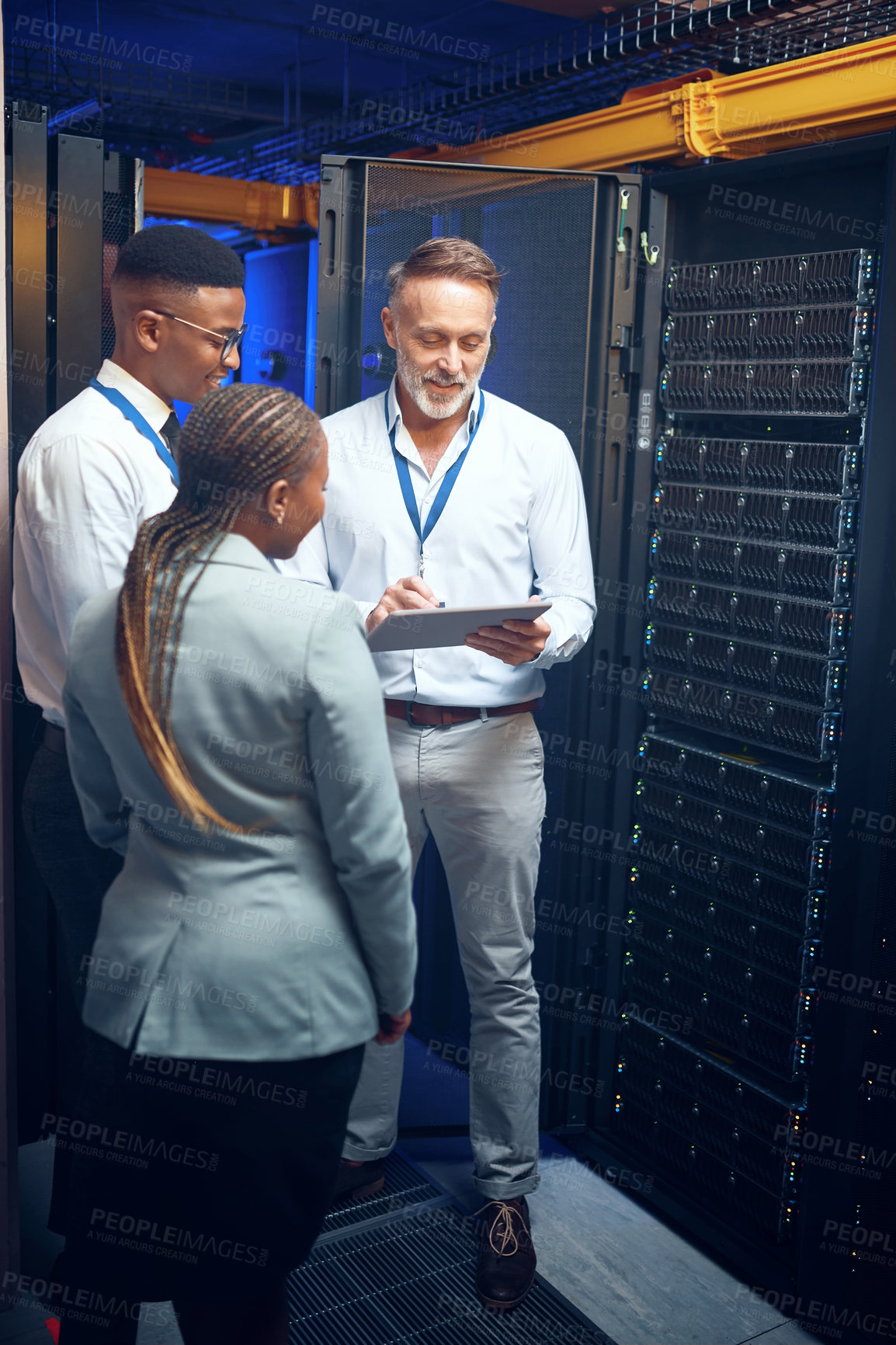 Buy stock photo Shot of a group of technicians using a digital tablet while working together in a server room