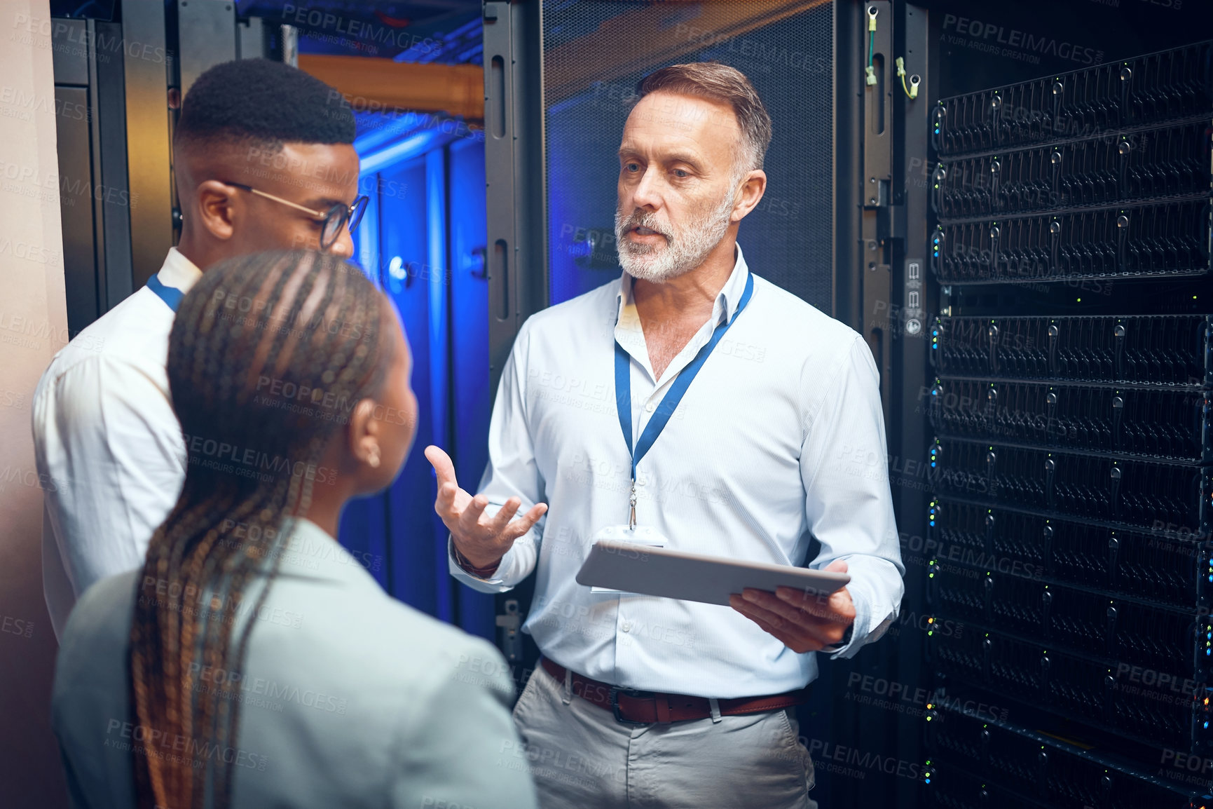 Buy stock photo Shot of a group of technicians using a digital tablet while working together in a server room