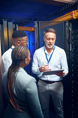 Buy stock photo Shot of a group of technicians using a digital tablet while working together in a server room