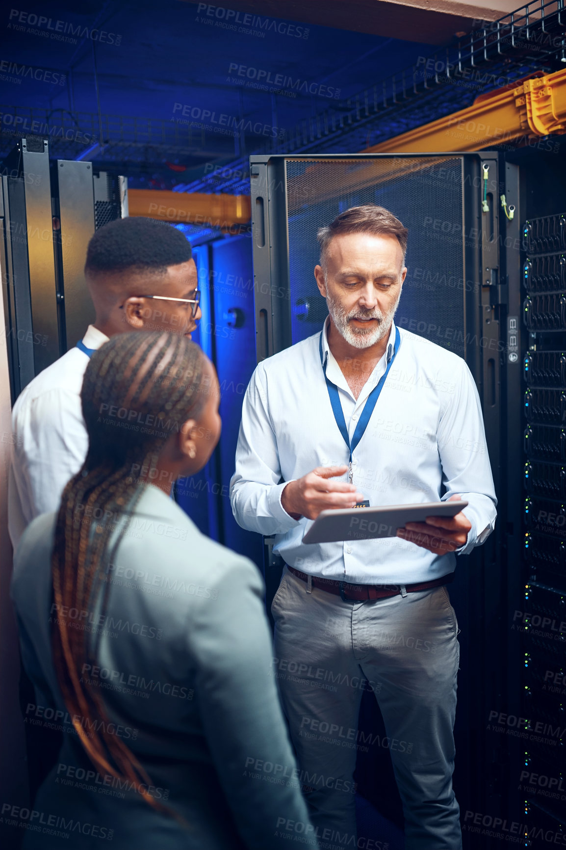 Buy stock photo Shot of a group of technicians using a digital tablet while working together in a server room