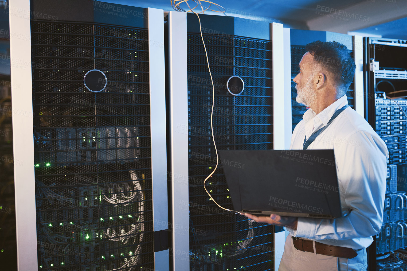 Buy stock photo Shot of a mature man using a laptop while working in a server room