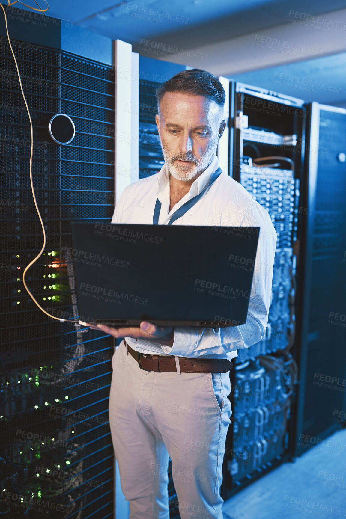 Buy stock photo Shot of a mature man using a laptop while working in a server room