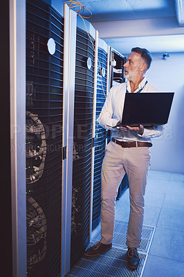 Buy stock photo Shot of a mature man using a laptop while working in a server room