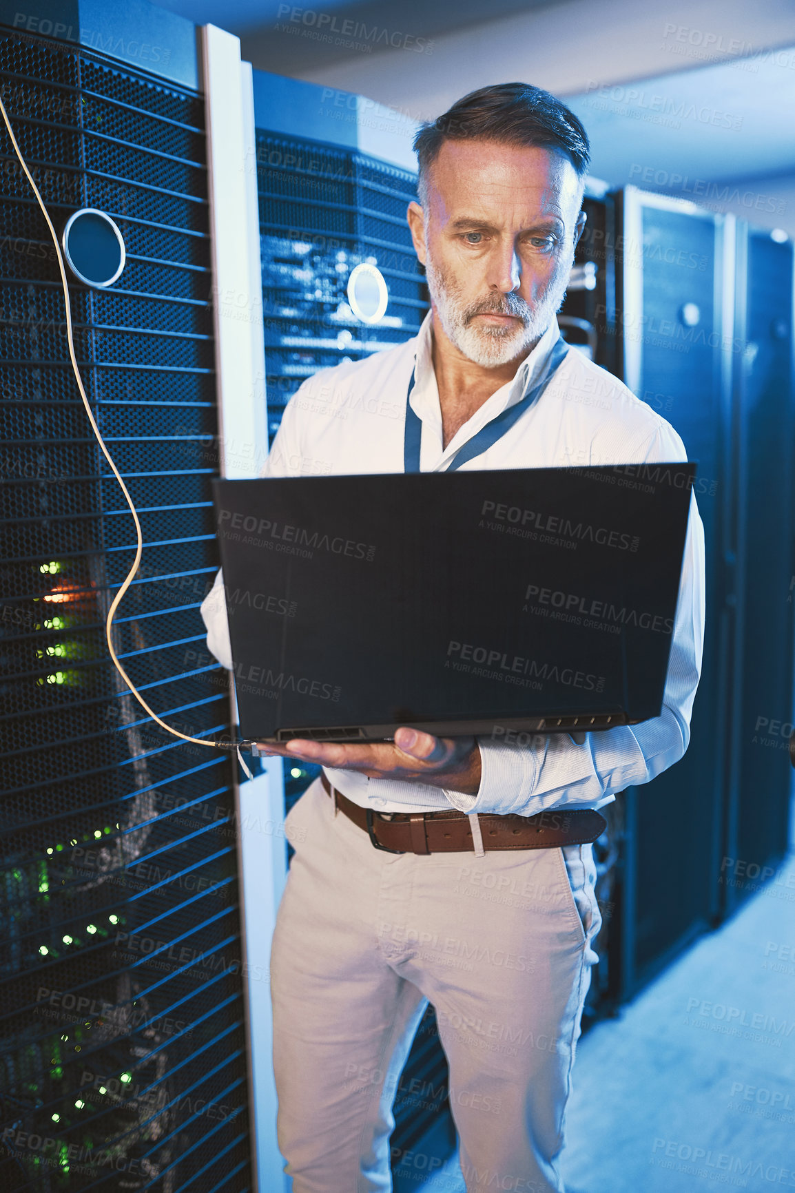 Buy stock photo Shot of a mature man using a laptop while working in a server room