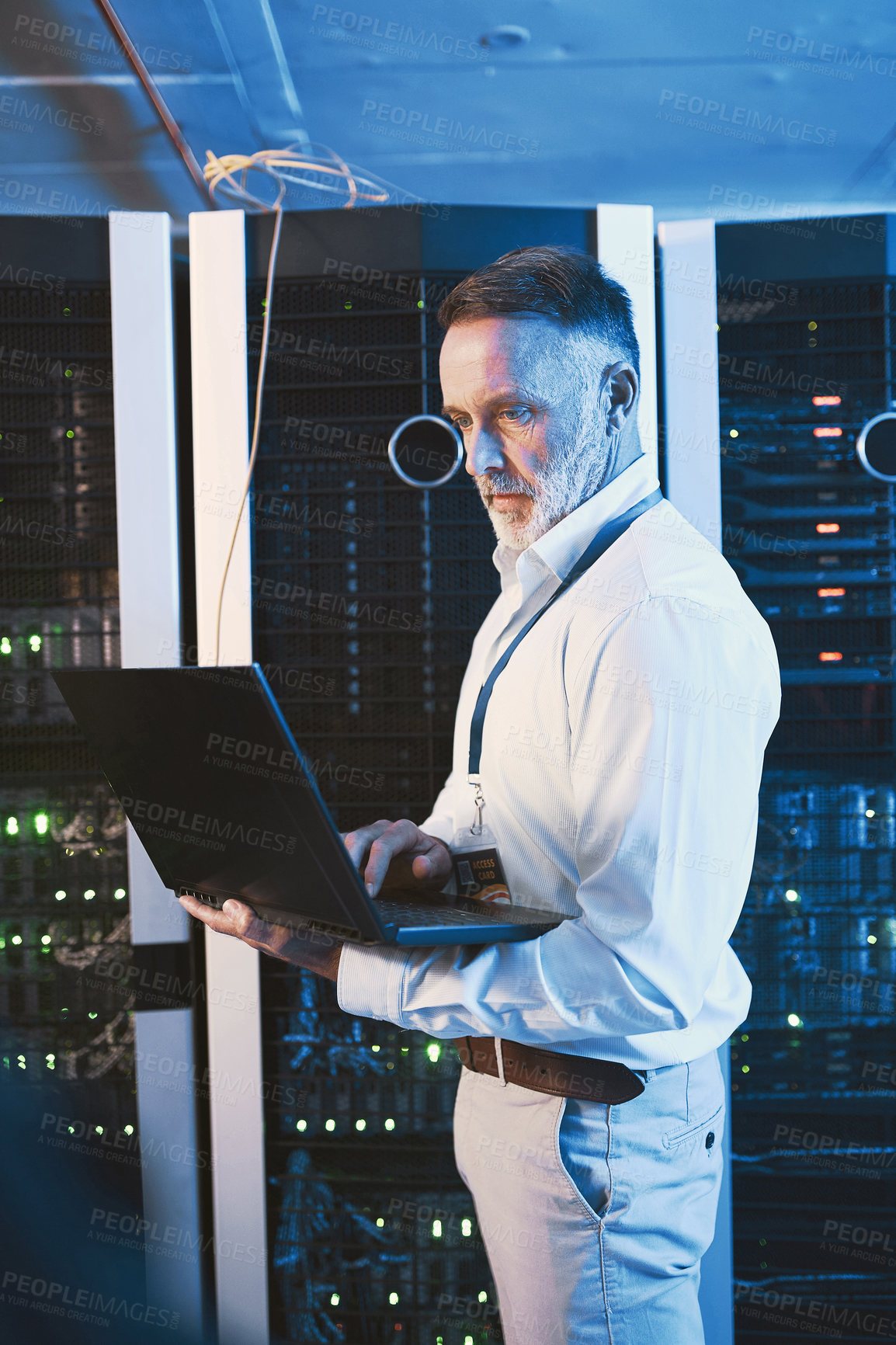 Buy stock photo Shot of a mature man using a laptop while working in a server room