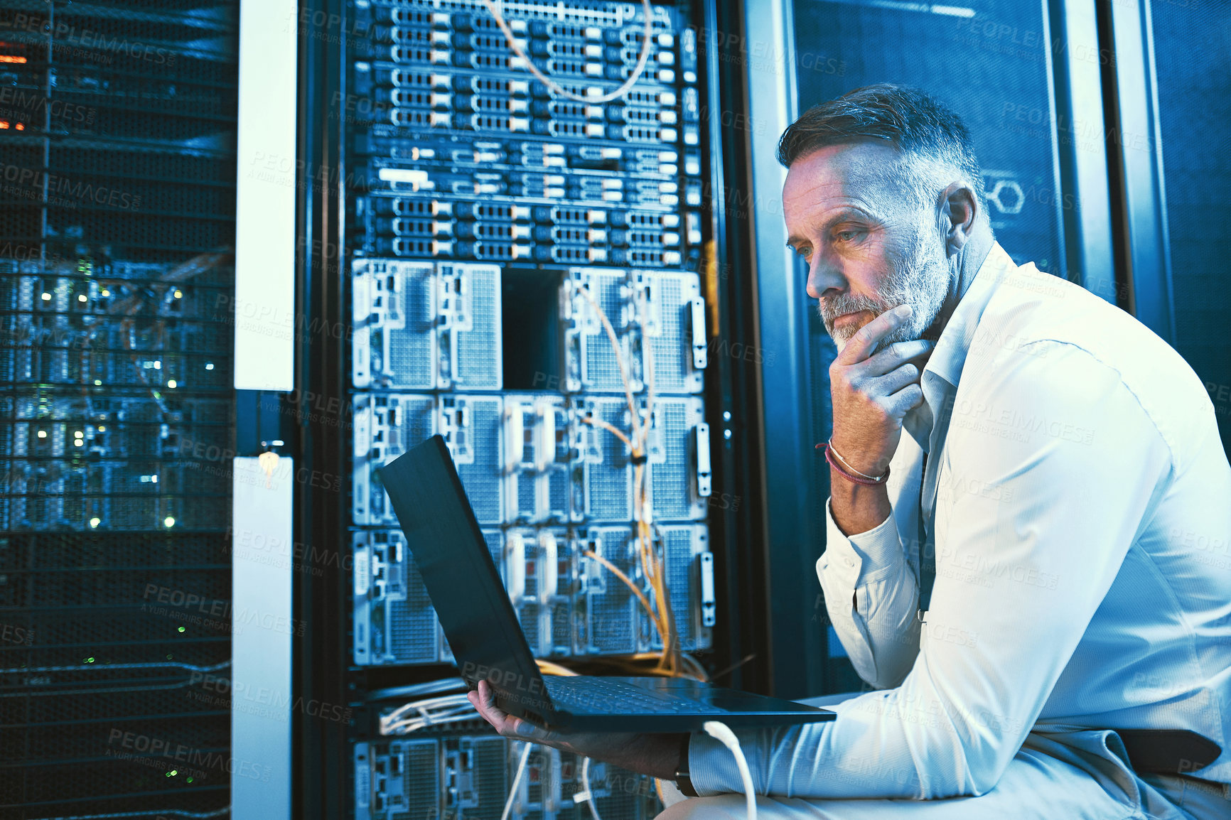 Buy stock photo Shot of a mature man looking thoughtful while using a laptop in a server room