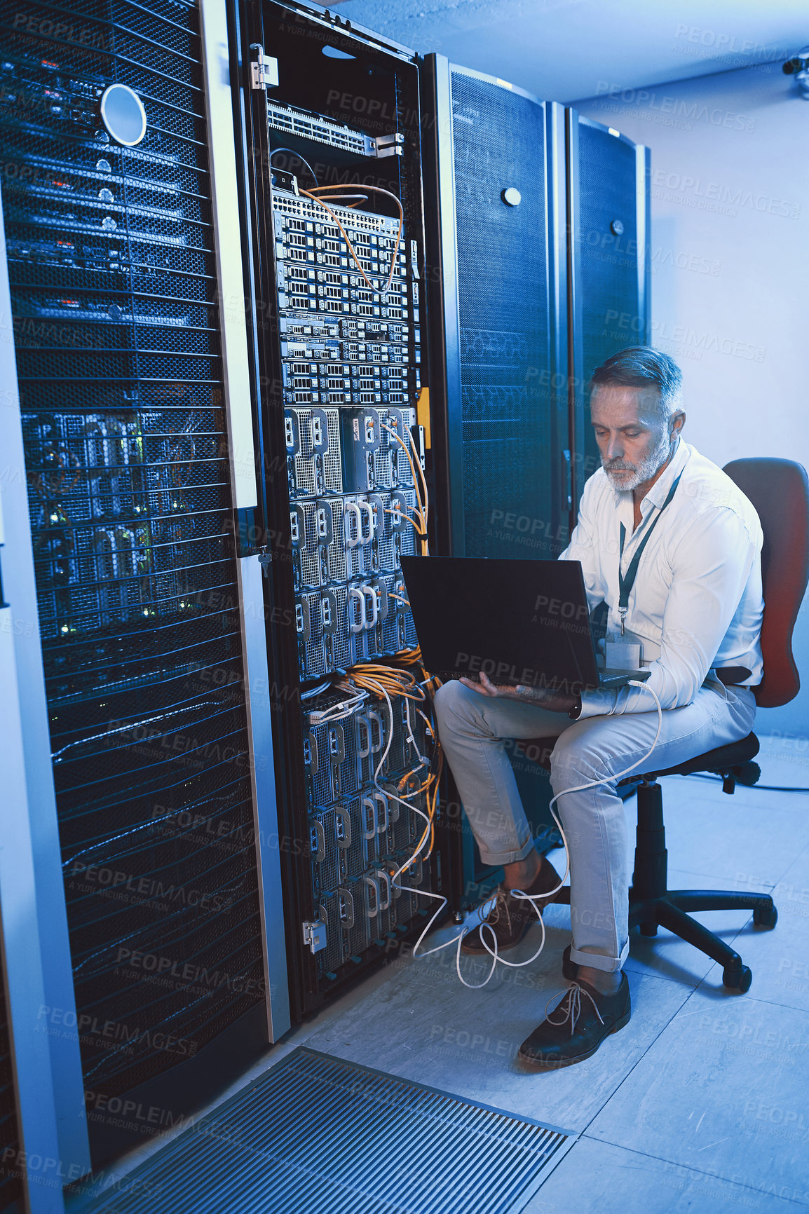 Buy stock photo Shot of a mature man using a laptop while working in a server room