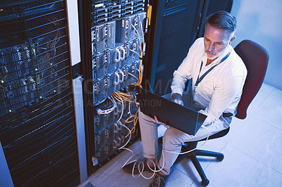 Buy stock photo High angle shot  of a mature man using a laptop while working in a server room