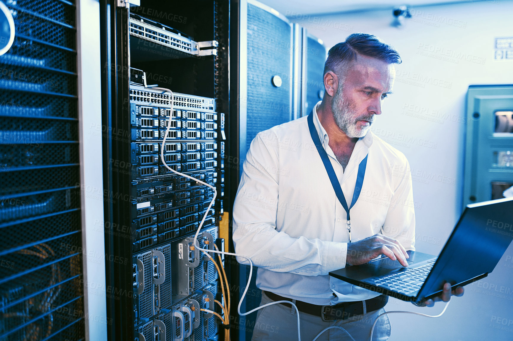 Buy stock photo Shot of a mature man using a laptop while working in a server room