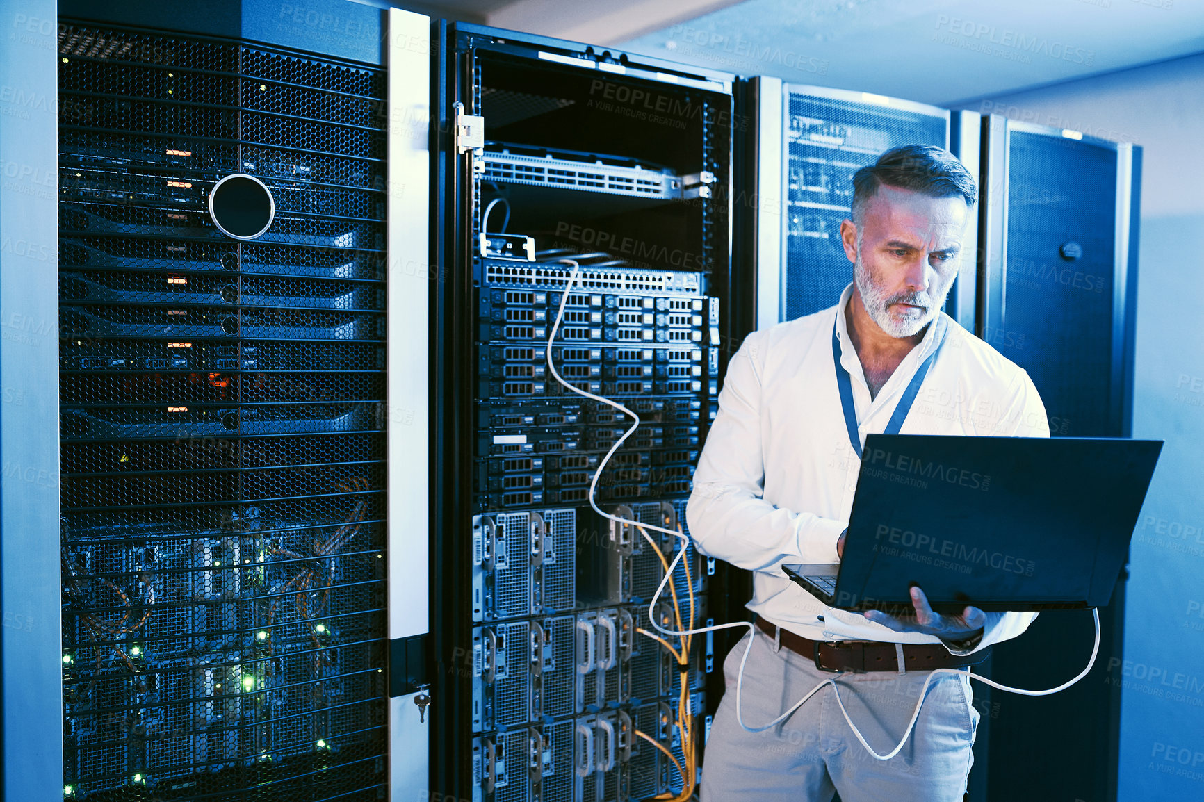 Buy stock photo Shot of a mature man using a laptop while working in a server room