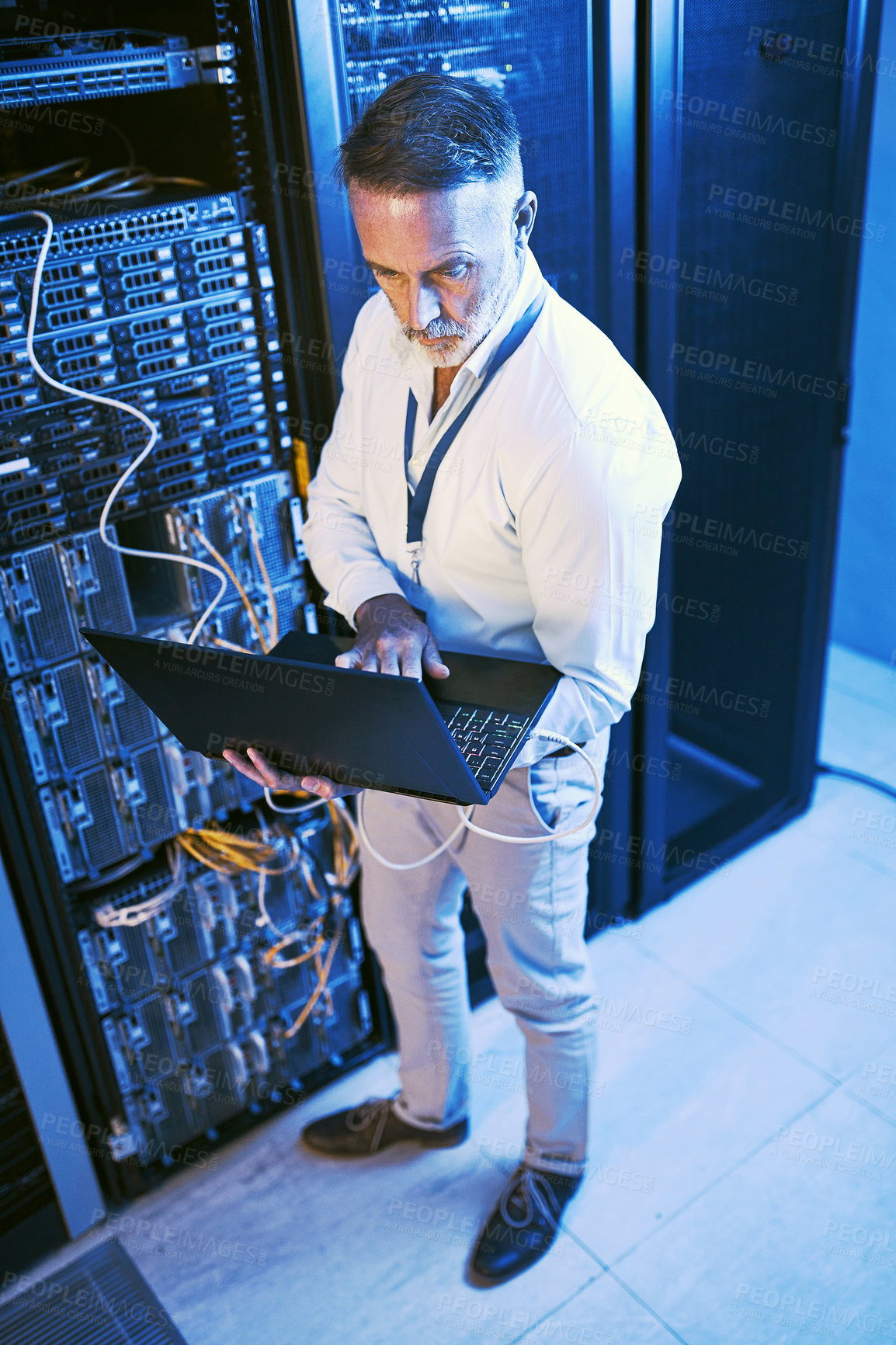 Buy stock photo High angle shot  of a mature man using a laptop while working in a server room