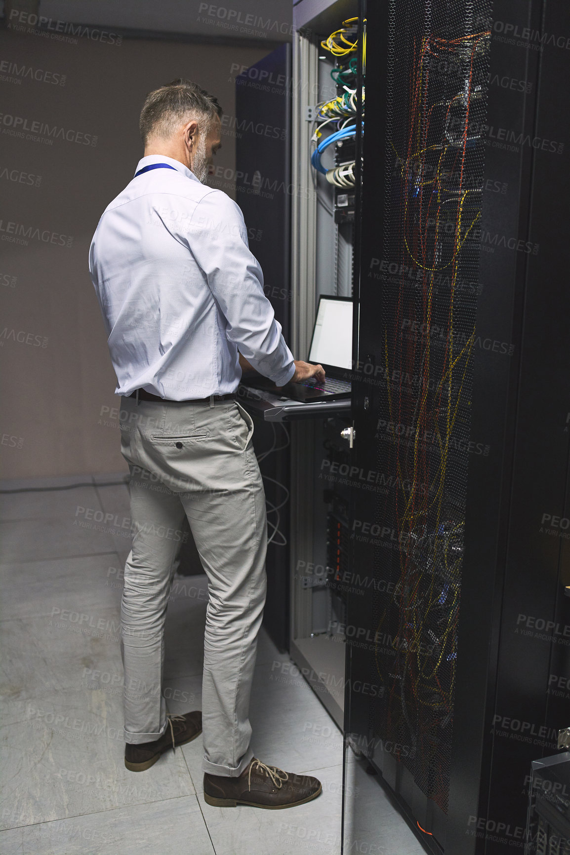 Buy stock photo Rearview shot of a mature man using a laptop while working in a server room