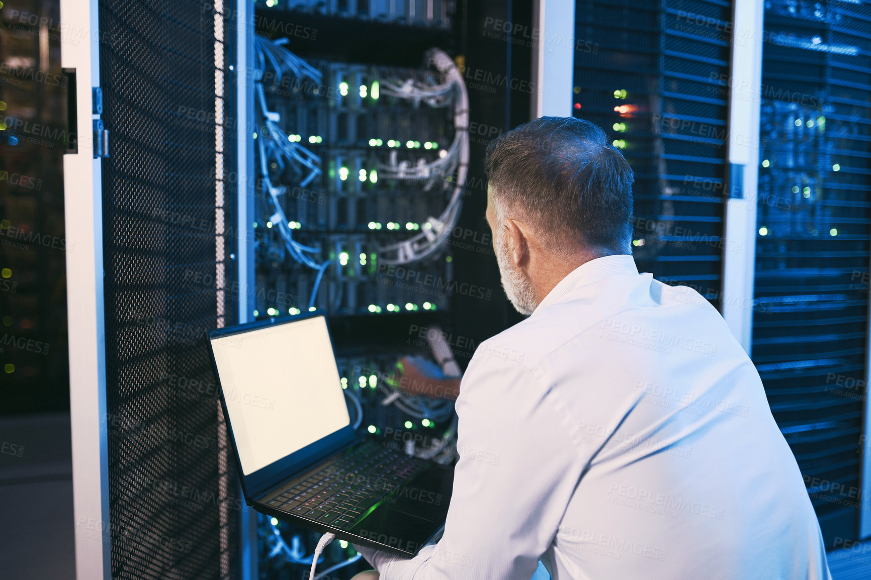 Buy stock photo Rearview shot of a mature man using a laptop while working in a server room