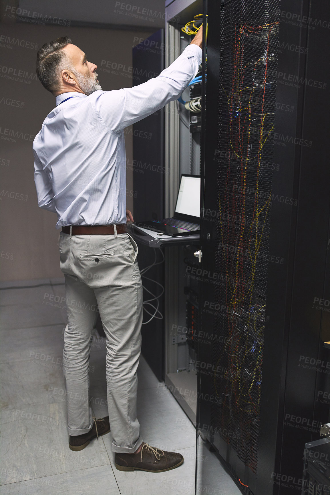 Buy stock photo Rearview shot of a mature man using a laptop while working in a server room