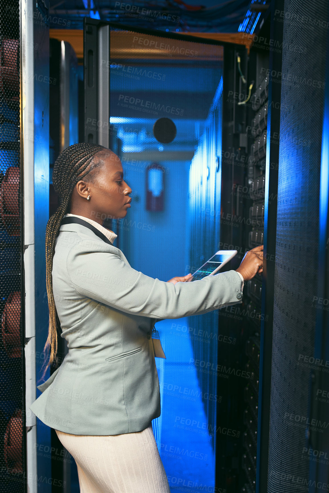 Buy stock photo Shot of a young IT specialist standing alone in the server room and using a digital tablet