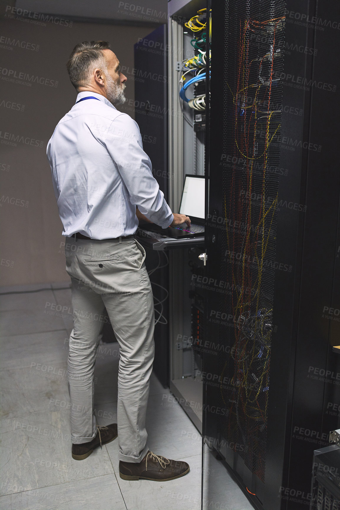 Buy stock photo Rearview shot of a mature man using a laptop while working in a server room