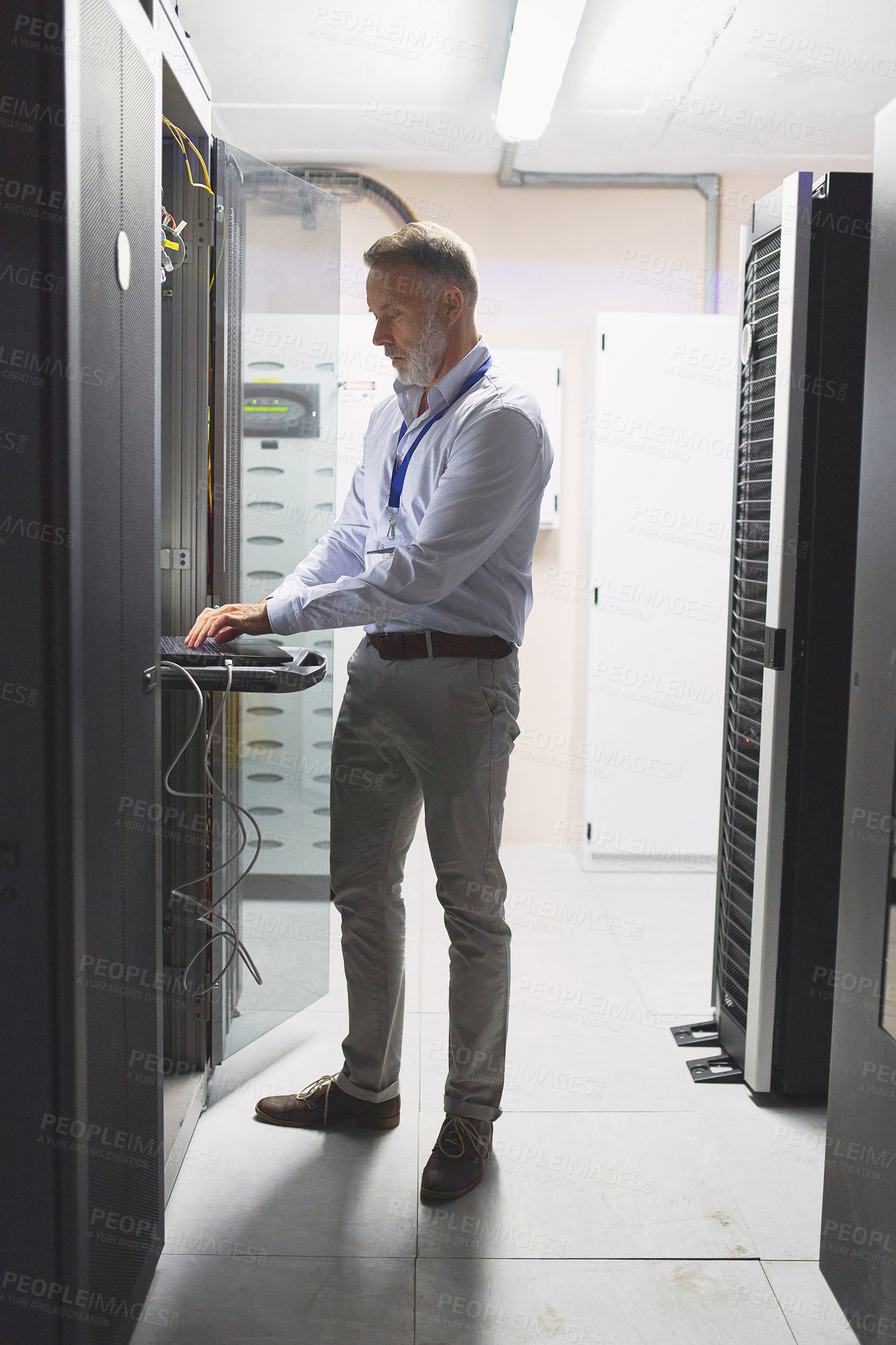 Buy stock photo Shot of a mature man using a laptop while working in a server room