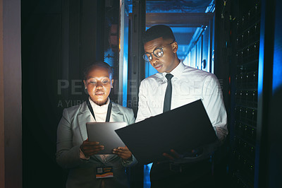 Buy stock photo Shot of two young IT specialists standing in the server room and having a discussion while using a technology