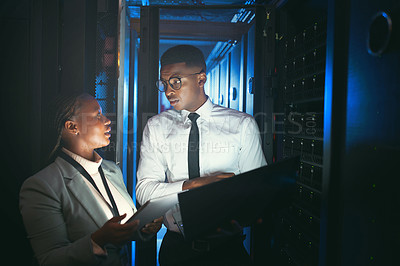 Buy stock photo Shot of two young IT specialists standing in the server room and having a discussion while using a technology