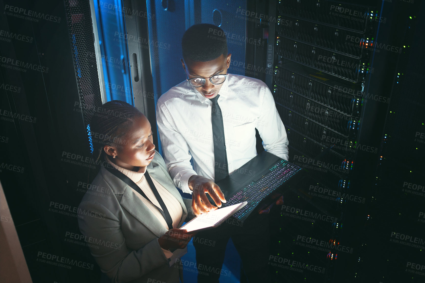 Buy stock photo Shot of two young IT specialists standing in the server room and having a discussion while using a technology