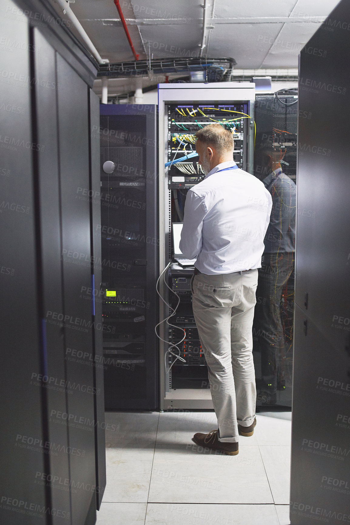 Buy stock photo Rearview shot of a mature man using a laptop while working in a server room