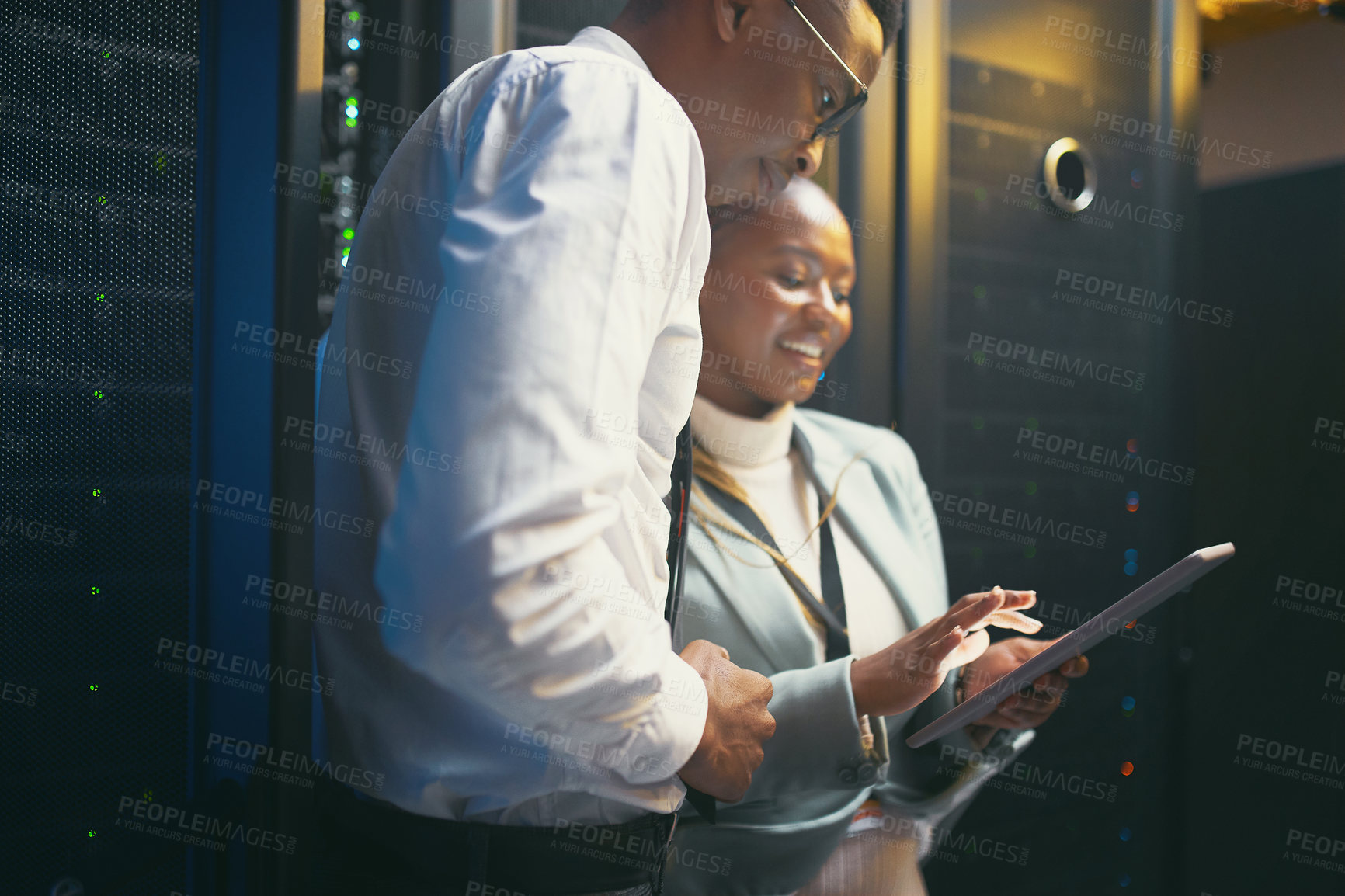 Buy stock photo Shot of two young IT specialists standing in the server room and having a discussion while using a digital tablet