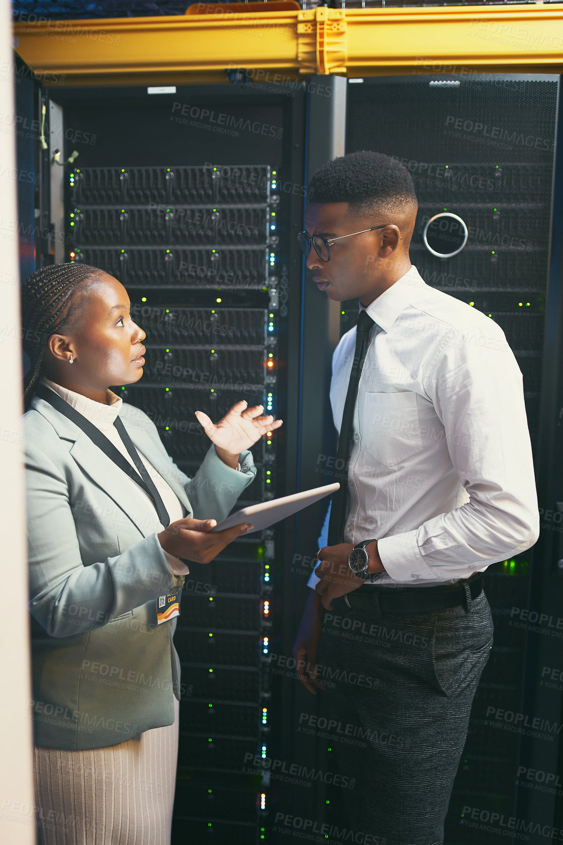 Buy stock photo Shot of two young IT specialists standing in the server room and having a discussion while using a digital tablet