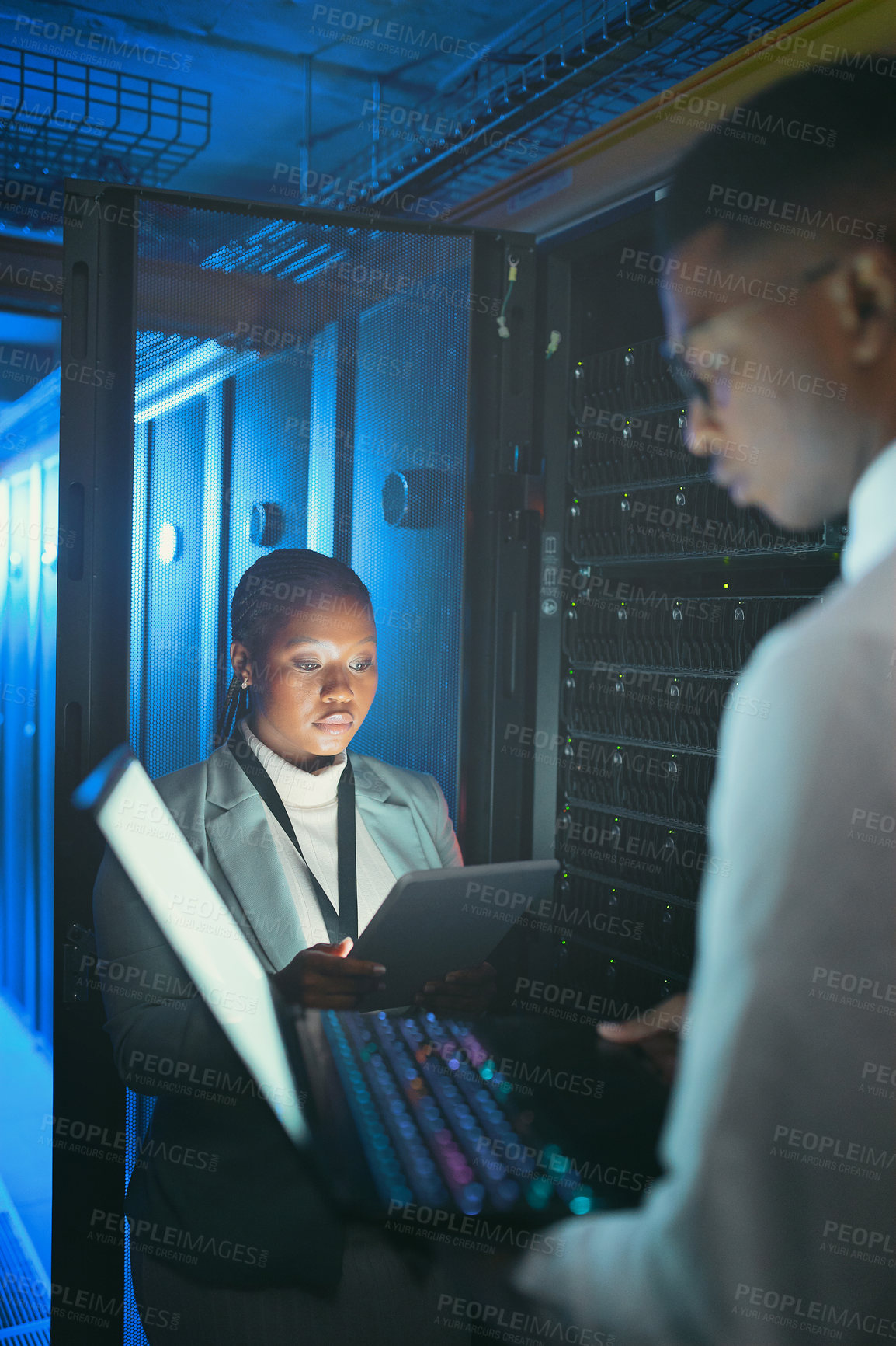 Buy stock photo Shot of two young IT specialists standing in the server room and using a technology