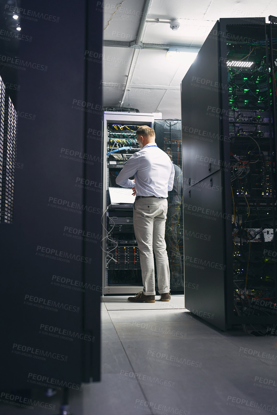 Buy stock photo Rearview shot of a mature man using a laptop while working in a server room