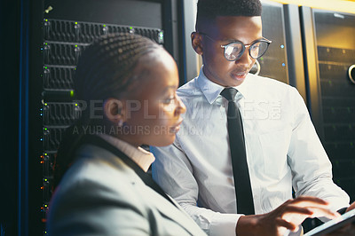 Buy stock photo Shot of two young IT specialists standing in the server room and having a discussion while using a digital tablet