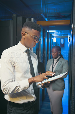 Buy stock photo Shot of two young IT specialists standing together in the server room and using technology