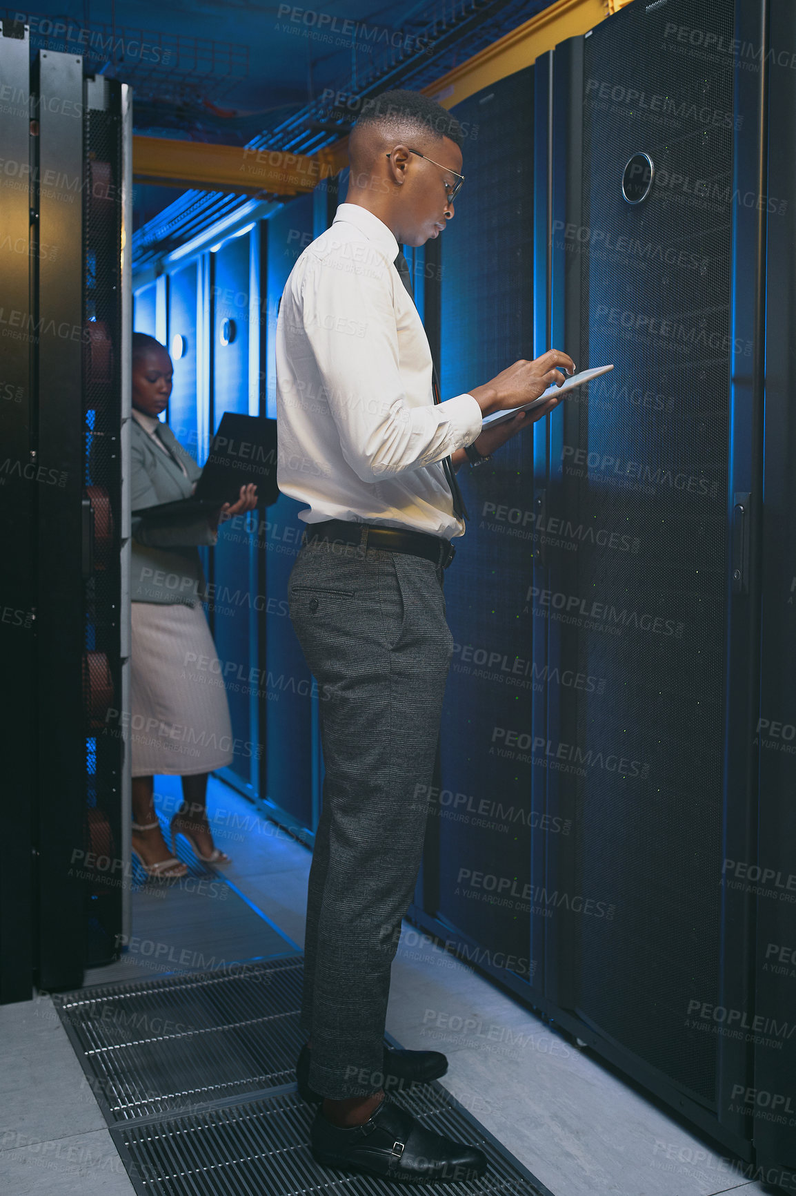 Buy stock photo Shot of two young IT specialists standing together in the server room and using technology