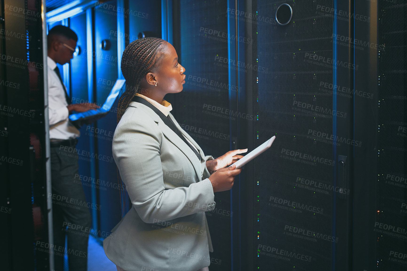 Buy stock photo Shot of two young IT specialists standing together in the server room and using technology