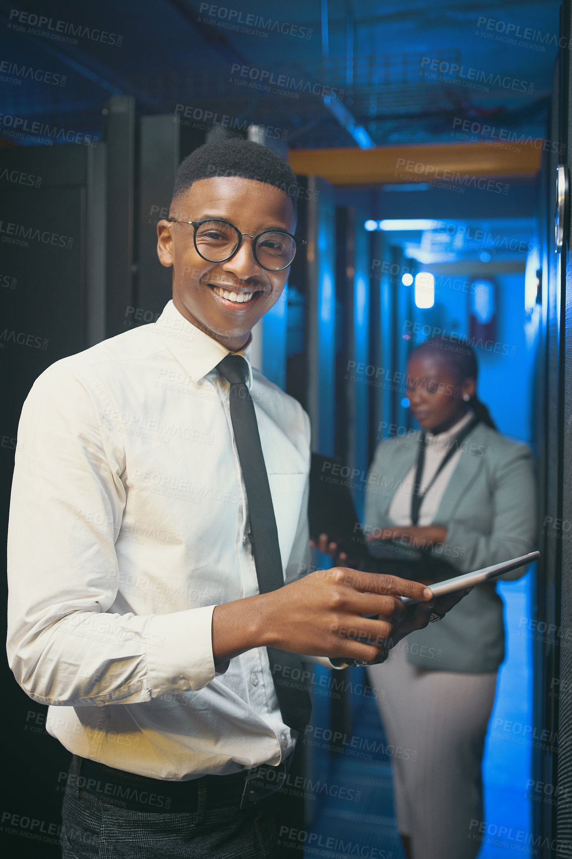 Buy stock photo Shot of two young IT specialists standing together in the server room and using technology