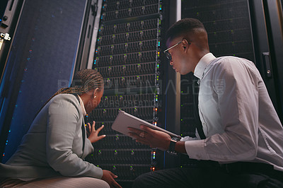 Buy stock photo Shot of two young IT specialists crouched down in the server room together and using a digital tablet