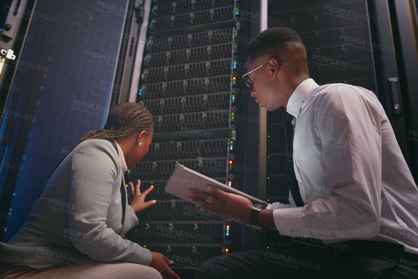 Buy stock photo Shot of two young IT specialists crouched down in the server room together and using a digital tablet