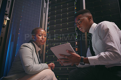 Buy stock photo Shot of two young IT specialists crouched down in the server room together and using a digital tablet