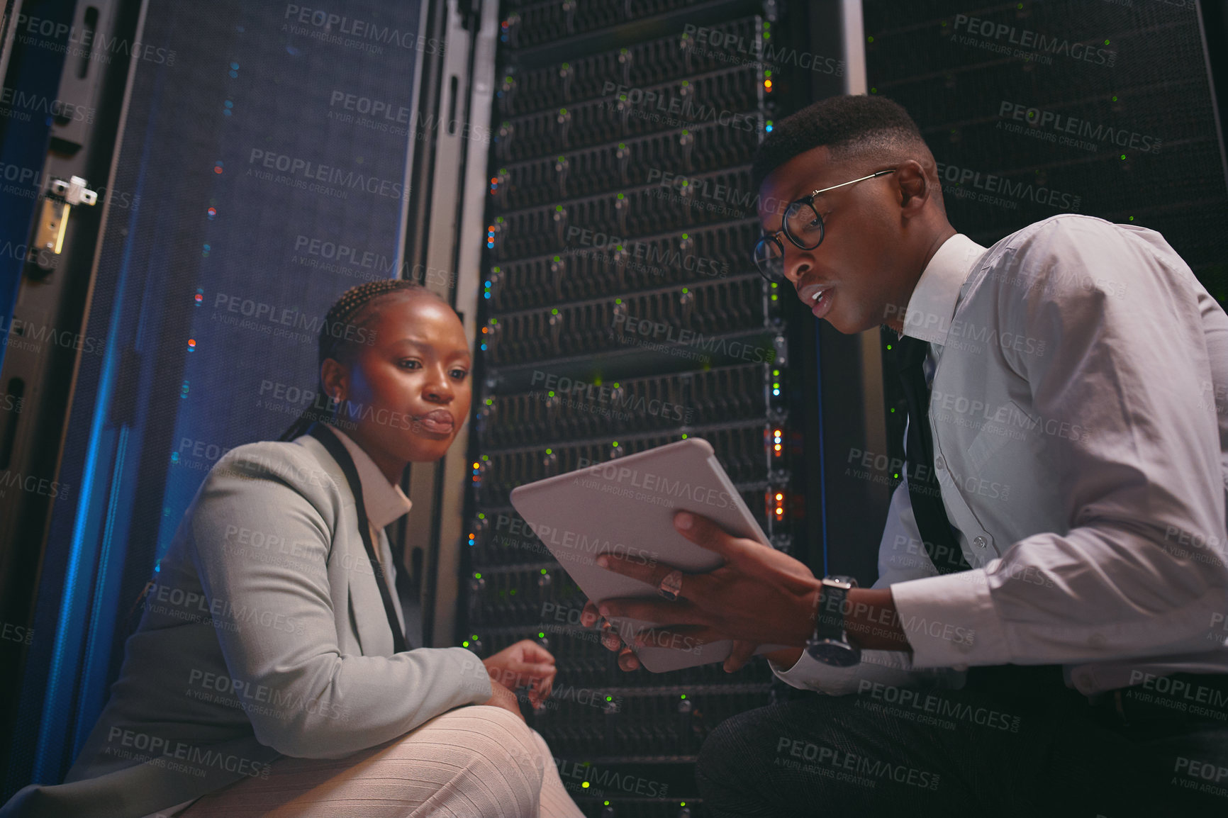 Buy stock photo Shot of two young IT specialists crouched down in the server room together and using a digital tablet