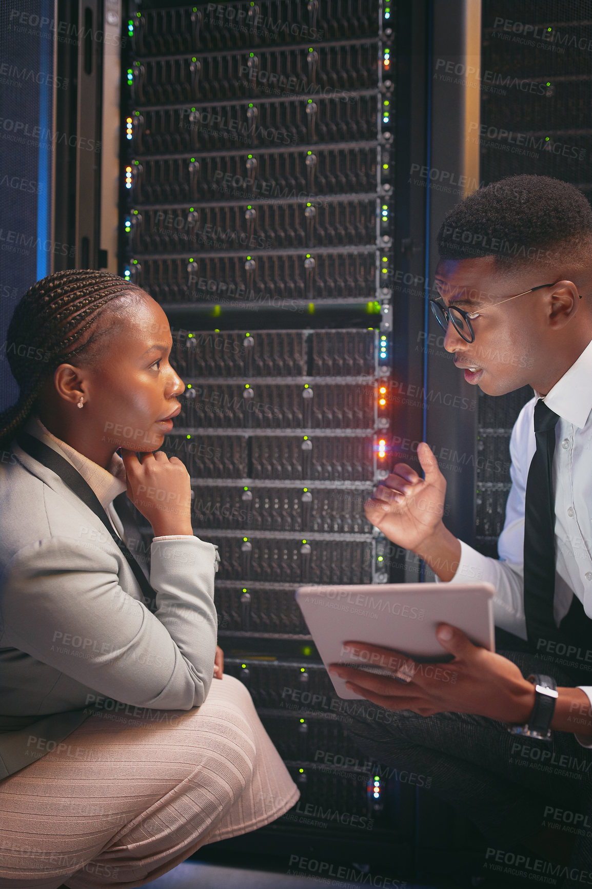 Buy stock photo Shot of two young IT specialists crouched down in the server room together and using a digital tablet