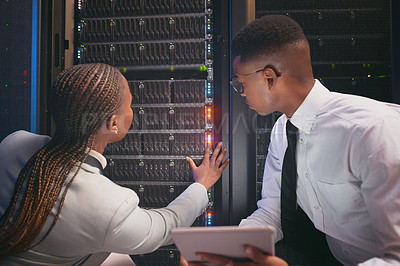 Buy stock photo Shot of two young IT specialists crouched down in the server room together and using a digital tablet