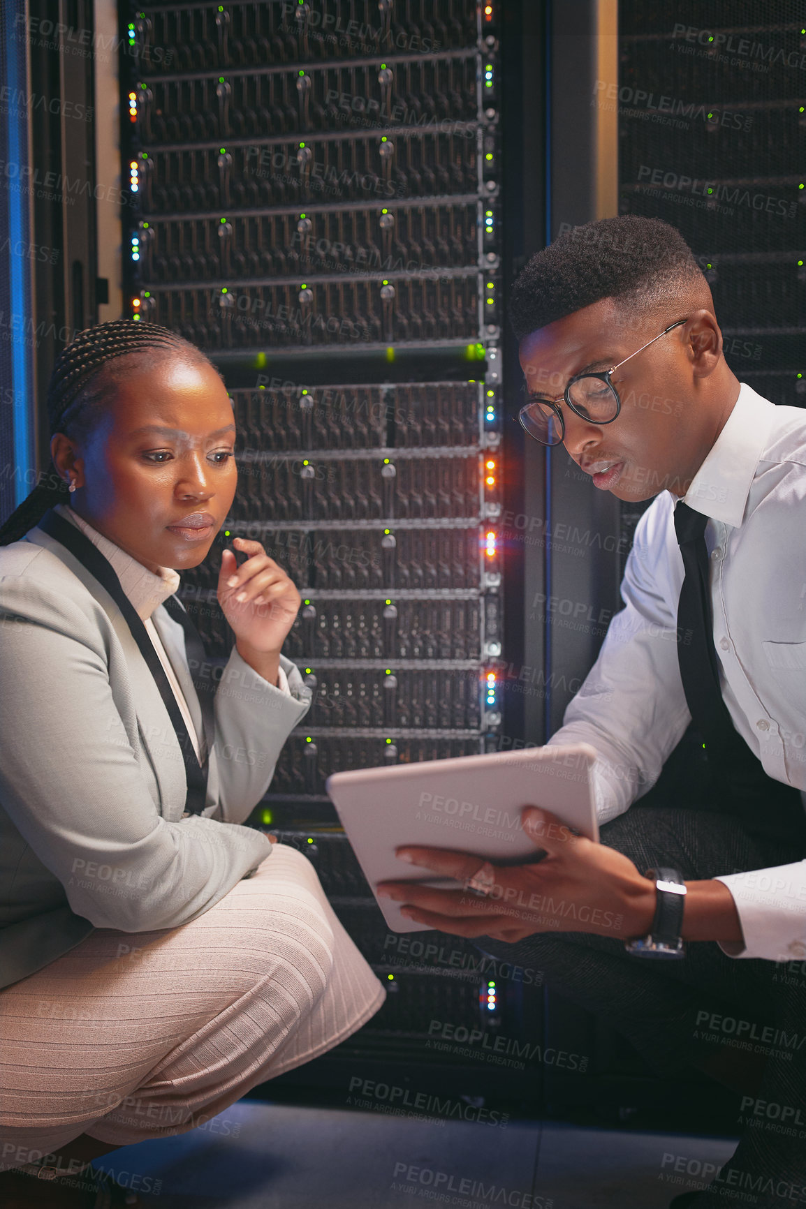 Buy stock photo Shot of two young IT specialists crouched down in the server room together and using a digital tablet