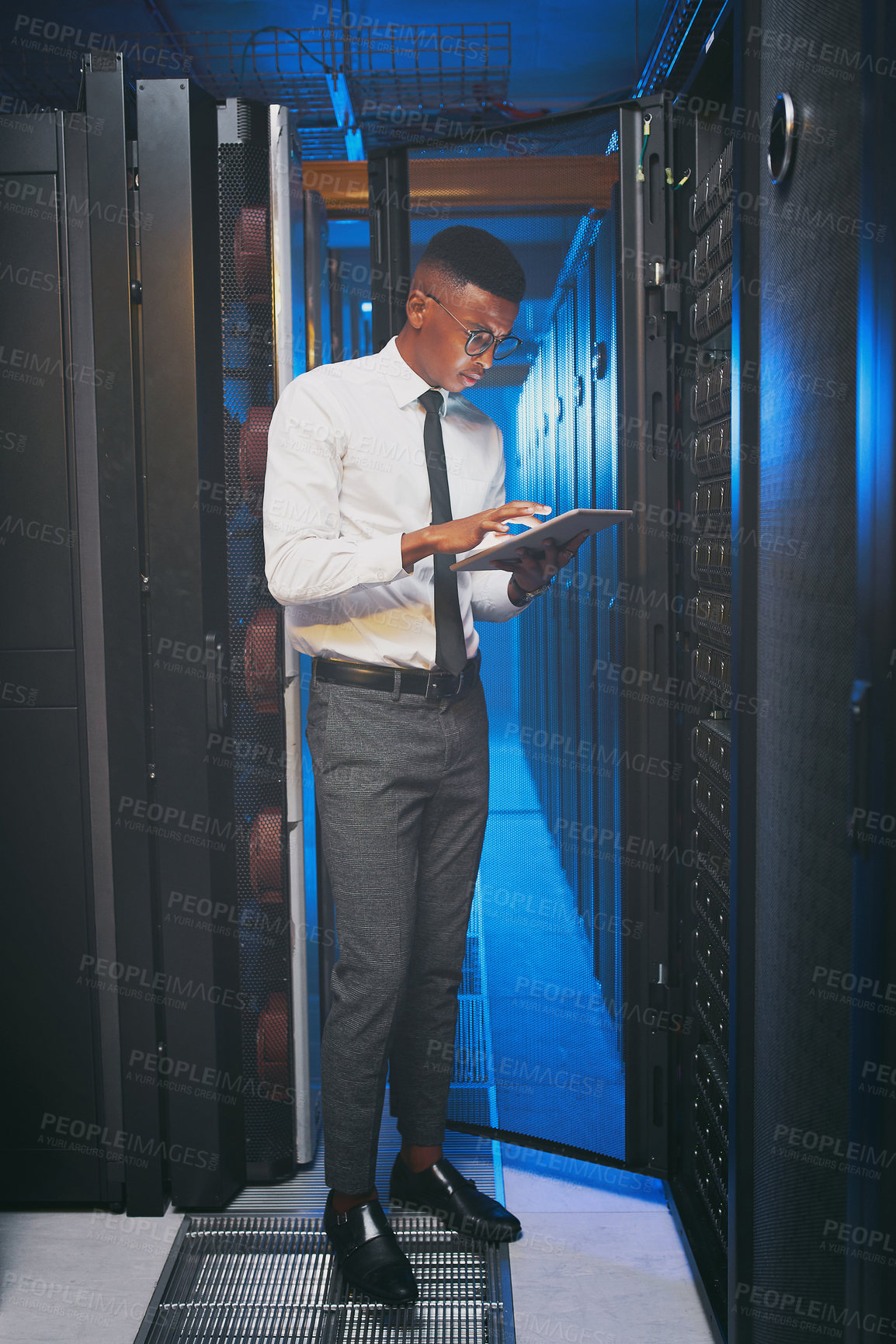 Buy stock photo Full length shot of a young IT specialist standing alone in the server room and using a digital tablet